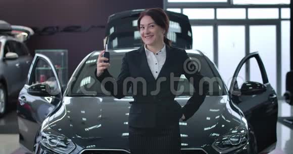 阳性的成年白种人妇女在新的黑色汽车前摆着车钥匙快乐车主站着视频的预览图