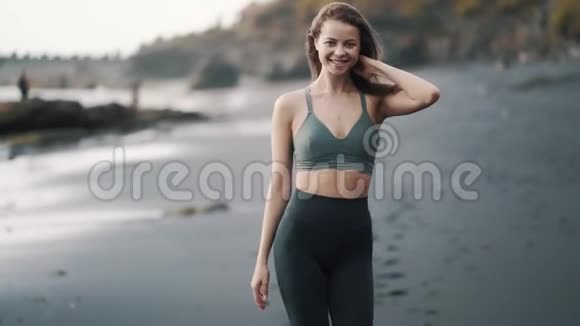 穿着运动服的女人走在黑沙滩上看着镜头微笑着视频的预览图