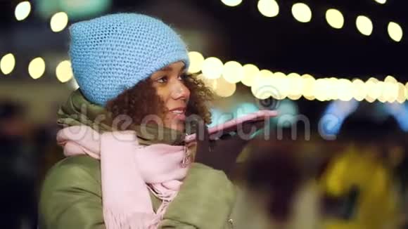 欢乐的黑人女孩在夜间灯光闪烁的溜冰场打电话视频的预览图