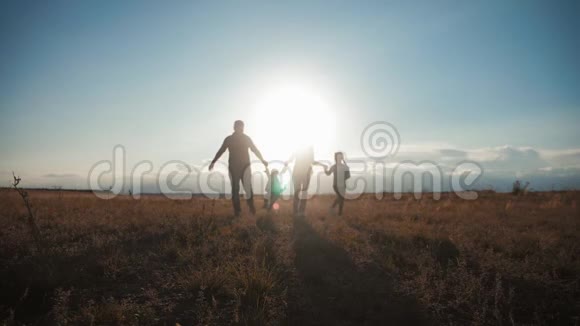 日落时和孩子们一起快乐的年轻家庭人们在夏日夕阳草地上剪影友好的概念视频的预览图
