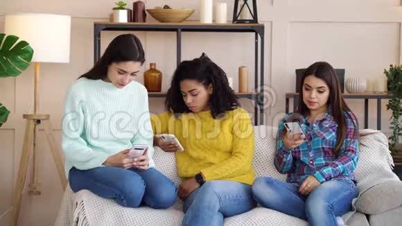 多种族女孩坐在客厅里使用智能手机视频的预览图