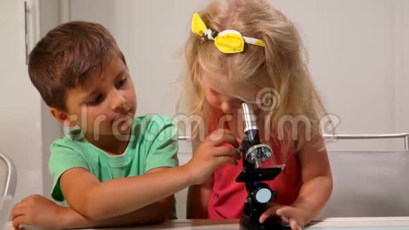 穿绿色t恤的男孩向一个可爱的小女孩展示了如何通过显微镜观察视频的预览图