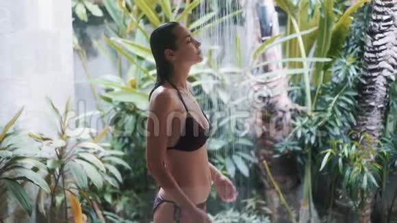 穿比基尼的苗条女孩接受绿色植物的清爽淋浴视频的预览图