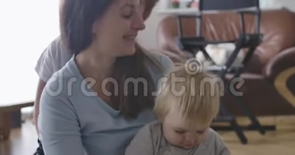 年轻的高加索母亲坐在地板上小女儿作为她的大儿子亲吻她的脸颊快乐的女人视频的预览图