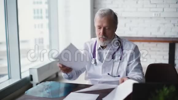 头发灰白的成年男性医生正在检查医疗文件视频的预览图