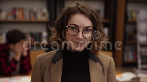 一位戴着眼镜长着短头发的欧洲女学生站在高中图书馆微笑着的肖像视频的预览图