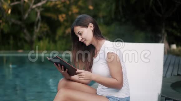 长头发的女孩在游泳池附近的菜单上选择菜视频的预览图