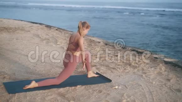 女人做瑜伽运动早上在海滩的垫子上做伸展运动视频的预览图