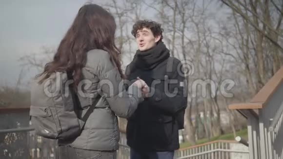 镜头远离快乐的年轻白种人男孩与女友在阳光明媚的秋天公园交谈快乐的黑发男人视频的预览图