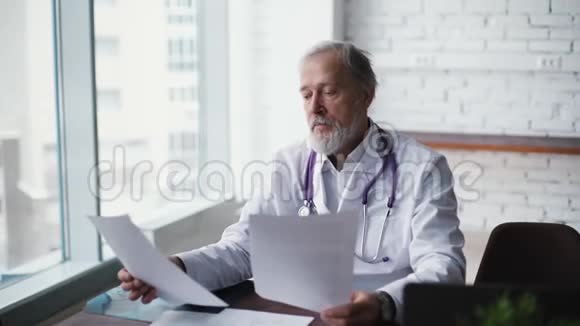 有经验的白种人成人医生坐在办公桌前研究病人报告视频的预览图