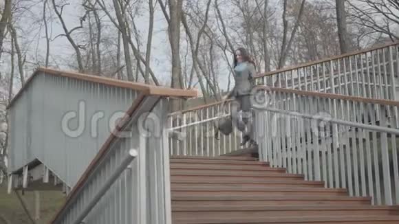 快乐的年轻白种人女人从城市公园的楼梯上跑下来抓背包然后离开快乐视频的预览图