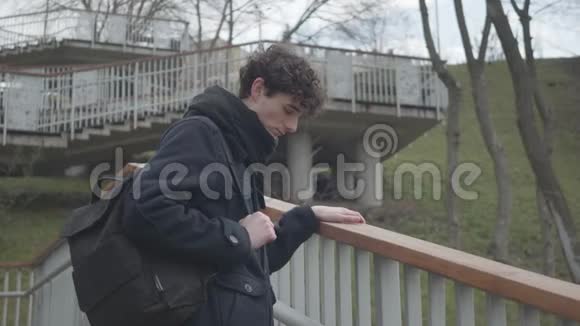 侧面观看悲伤的白人男孩与背包站在楼梯在城市公园和思考不快乐的男大学生视频的预览图