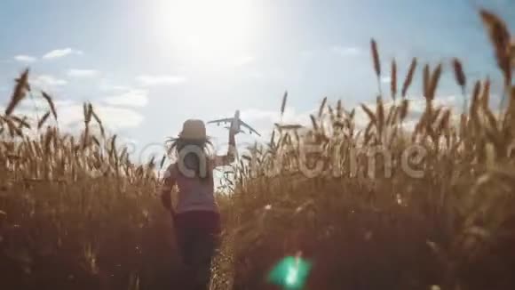 可爱的女孩在日落时在麦田里玩玩具飞机儿童玩玩具飞机的剪影视频的预览图