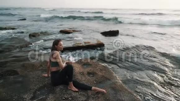 女孩在日落时分站在石头上与海浪搏斗视频的预览图