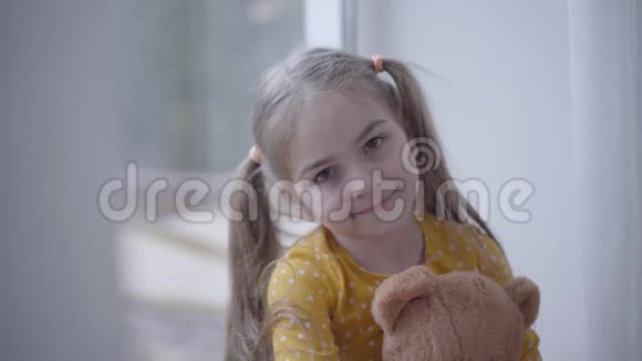 可爱的小女孩的特写肖像穿着黄色点缀的连衣裙抱着泰迪熊可爱的白人小孩抱着玩具视频的预览图