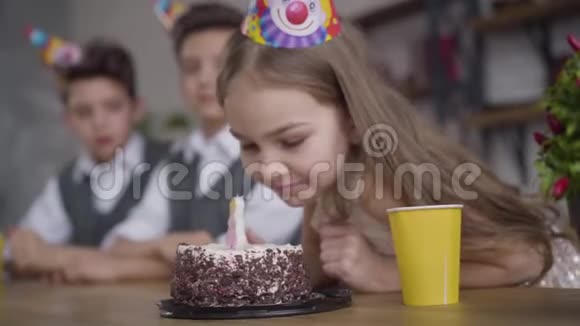 侧视特写滑稽的小白种人女孩咬着生日蛋糕模糊的孪生兄弟从她身上看她视频的预览图