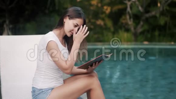 美丽的女孩在游泳池附近的菜单上选择菜视频的预览图