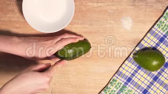 女人手切熟牛油果把一半放在桌子上在木制背景上烹饪鳄梨酱从上面看视频的预览图