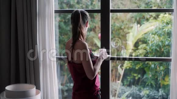 从侧面看穿睡衣的女人早上喝咖啡看着窗外视频的预览图