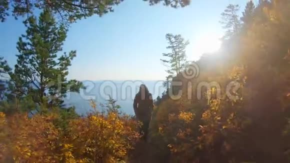 女孩在阳光明媚的秋日爬上贝加尔湖岸陡坡的小路视频的预览图