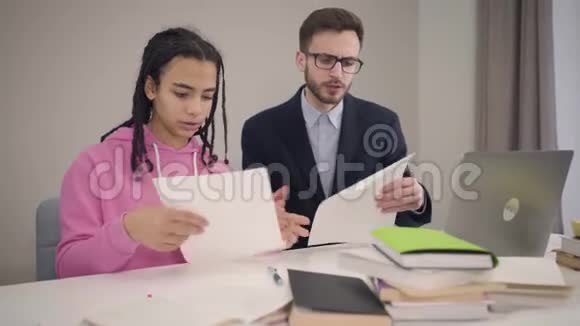 镜头慢慢接近非裔美国女孩和白人男孩翻阅文件帮助青年学生视频的预览图