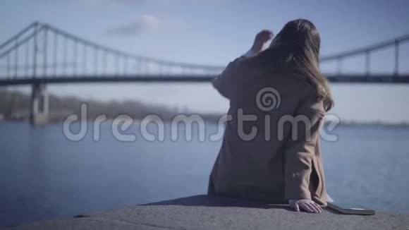 黑黑肤色白种人女人的后景秋衣坐在河岸上看波浪冷静的年轻姑娘视频的预览图