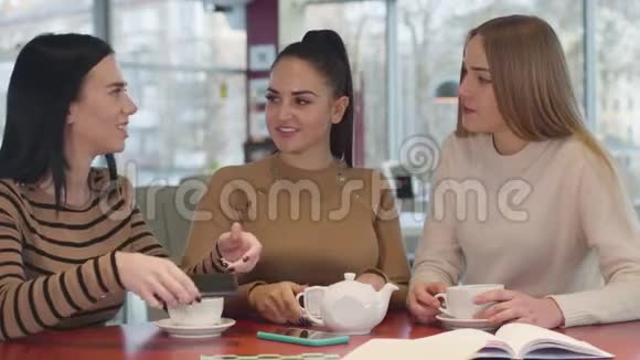 特写三位高加索女性朋友在餐厅看智能手机屏幕和交谈年轻女人说闲话视频的预览图