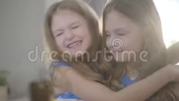 幸福的小漂亮女孩的特写脸拥抱双胞胎妹妹亲吻她的脸颊两个孩子在阳光下摆姿势视频的预览图