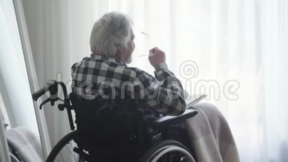 老人戴眼镜和看书的背面视图残疾退休老人视频的预览图