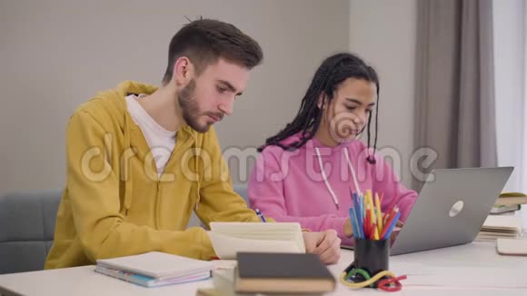 两个疲惫的多民族伙伴坐在桌边学习的肖像年轻的白人男孩打哈欠非洲人视频的预览图