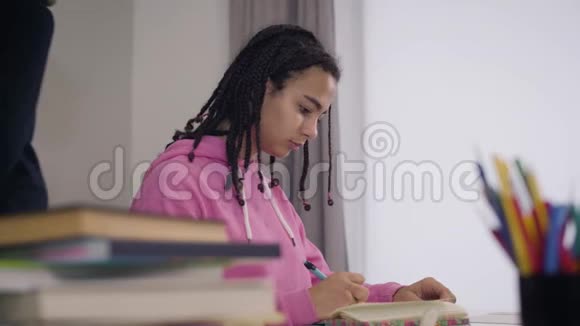 年轻的非裔美国女孩坐在桌子旁写下老师讲座穿西装的白人男教师视频的预览图