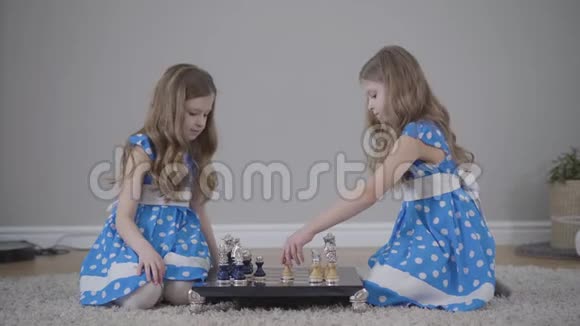 侧面看两个集中的白种人姐妹下棋聚焦双胞胎坐在对方面前的画像视频的预览图