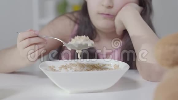 无聊得认不出来的小女孩用勺子拌麦片不快乐的中东孩子早上吃早餐视频的预览图