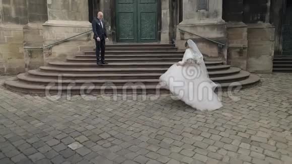 可爱的新娘在教堂附近的古楼梯上走向新郎视频的预览图