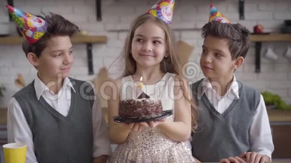 一个快乐的白种人女孩拿着生日蛋糕吹灭蜡烛两个兄弟站在一起视频的预览图