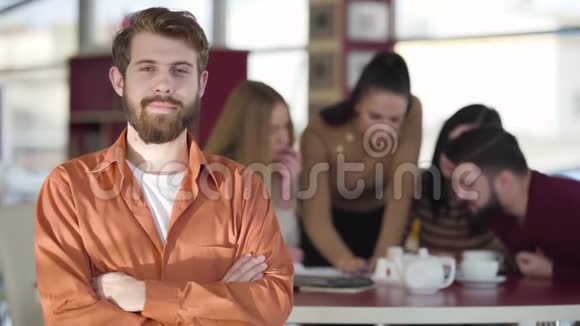 年轻的红头发白种人白种人的肖像他看着镜头微笑着他的朋友在后台学习视频的预览图