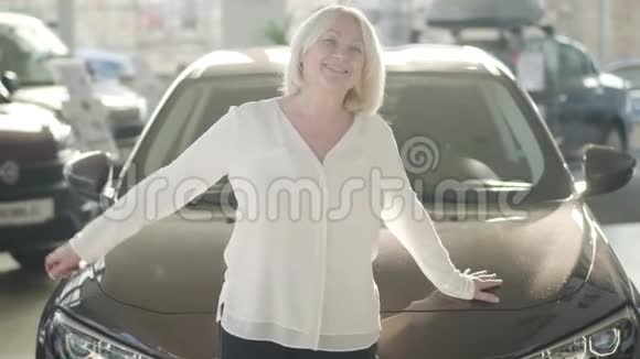 快乐成熟的白种人女人在新汽车旁边的经销商阳光下摆姿势的肖像快乐的高级夫人视频的预览图