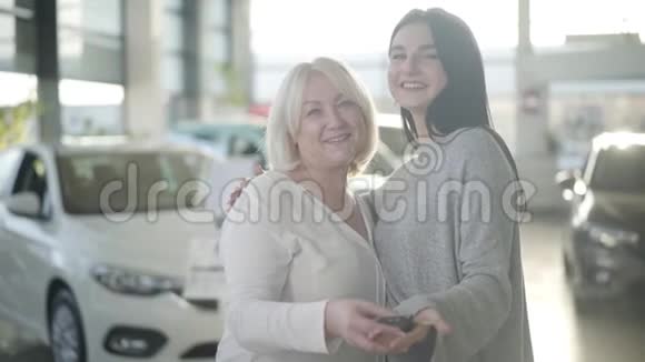 两个白人妇女拿着车钥匙看着相机微笑的肖像快乐的年长的金发母亲和年轻的视频的预览图