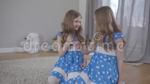 两个积极的白种人双胞胎姐妹穿着优雅的蓝色点缀连衣裙握住对方的小手指举起双手视频的预览图