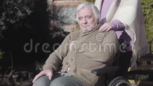 疲惫的老白种人残疾男子坐在轮椅上的户外牵着无法辨认的护士的手视频的预览图
