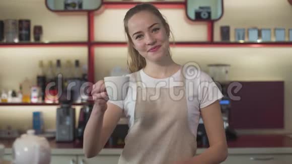 微笑着年轻的白种人女人在镜头前展示咖啡杯微笑着职业女性咖啡师在工作场所摆姿势视频的预览图