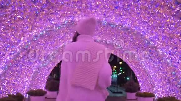 穿着白色毛衣和帽子的女人在夜晚穿过粉红色发光的隧道视频的预览图