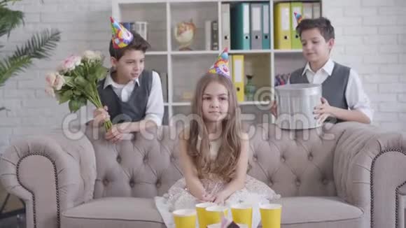 一幅美丽的小白种人女孩戴着派对帽从双胞胎兄弟那里收到一束玫瑰和礼物盒的肖像快乐视频的预览图