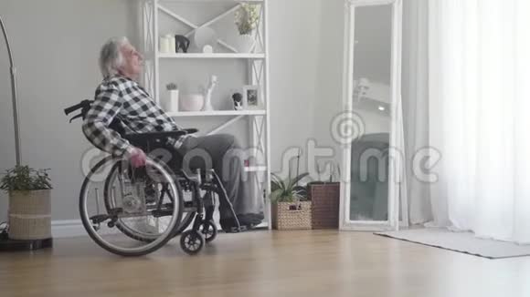 在家中坐在轮椅上的老白种人一边看着窗户沮丧的退休老人交手视频的预览图