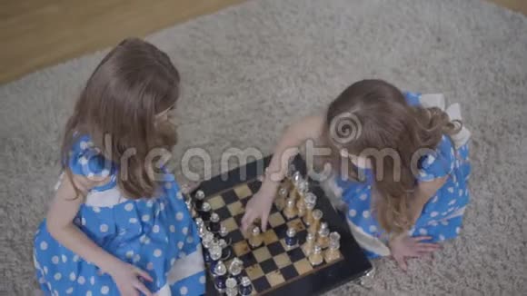 两个褐发白种人双胞胎姐妹在室内下棋的俯视图小女孩穿着优雅的蓝色衣服休息视频的预览图