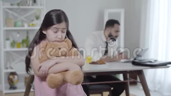 不高兴的小女孩回头看着忙碌的中东男人在笔记本电脑上打字然后转身回到相机伤心的女儿视频的预览图