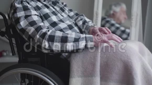 镜头接近无法辨认的男人手在颤抖坐在轮椅上思考的老年残疾人视频的预览图
