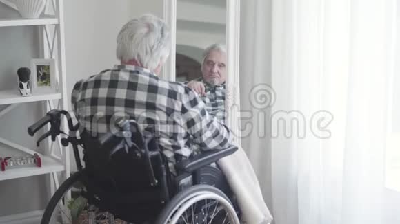 特写后景成熟的白种人坐在轮椅上看着镜子里的倒影悲伤的老年退休人员视频的预览图
