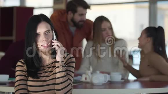年轻严肃的高加索女人在电话里聊天而她的朋友在咖啡馆的后台聊天自信的成年人视频的预览图