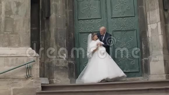 可爱的新娘和新郎在教堂附近的古老楼梯上视频的预览图